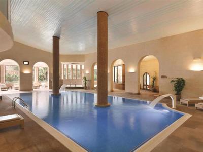 Vnitřní bazén v světlé, moderní místnosti se sloupy a pohodlnými lehátky.