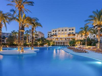 Hotel mit beleuchtetem Pool und Palmen in der Dämmerung