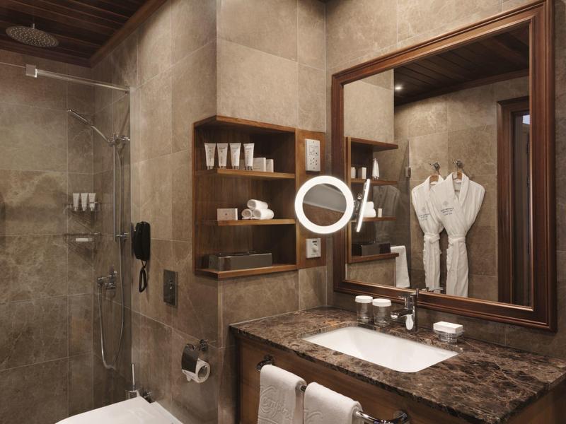 Elegantní koupelna s hnědou mramorovou deskou, zrcadlem, policemi a skleněnými dveřmi sprchy.