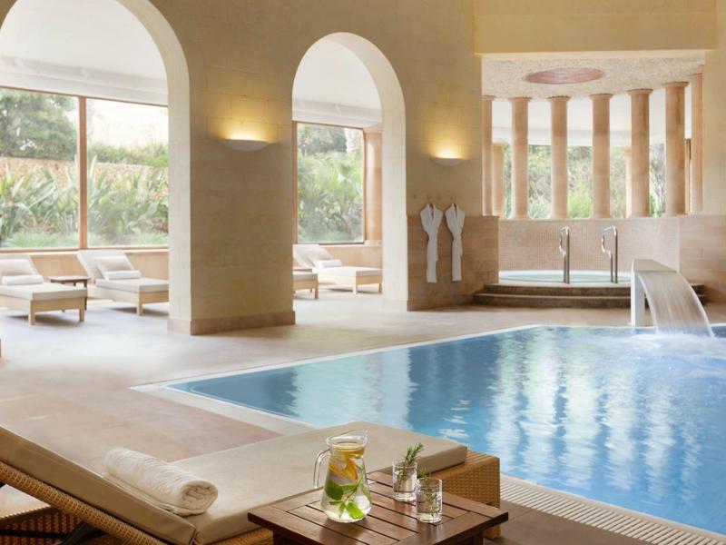 Vnitřní bazén s lehátky a velkými okny s výhledem na zahradu a terasu.