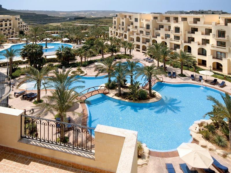 Velký bazén obklopený palmami a hotelovými budovami pod jasnou oblohou.