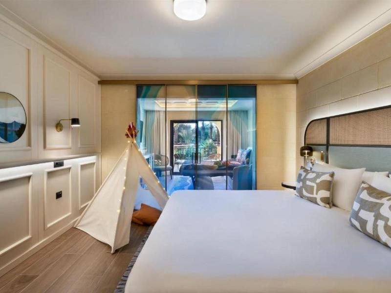 Moderně zařízený hotelový pokoj s velkou postelí, týpím a výhledem na balkon.