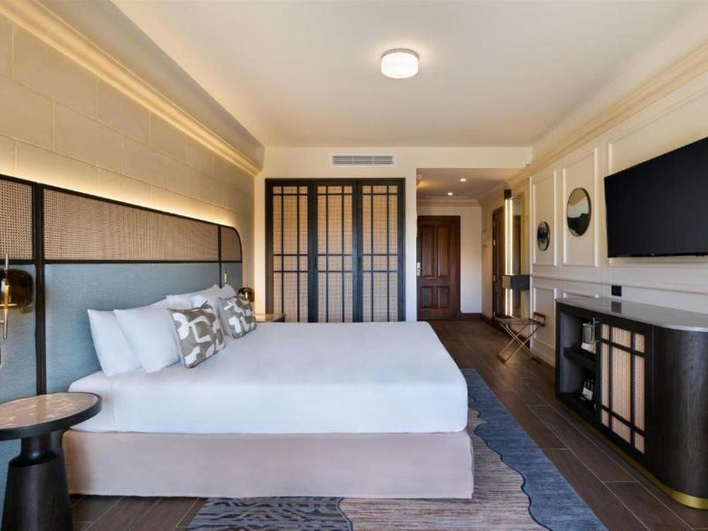 Moderní hotelový pokoj s velkou postelí, TV, skříní a stylovým nábytkem.