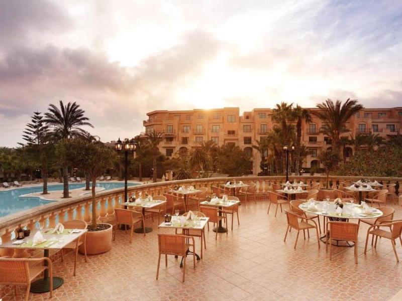 Terasa se stoly a židlemi vedle bazénu při západu slunce v hotelu.