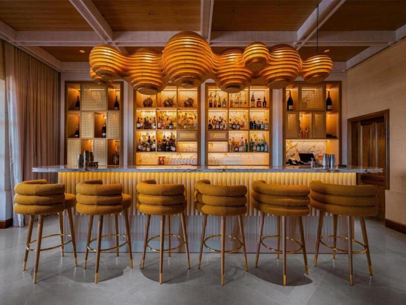 Elegantní hotelový bar se žlutými barovými židlemi a moderním stropním osvětlením.