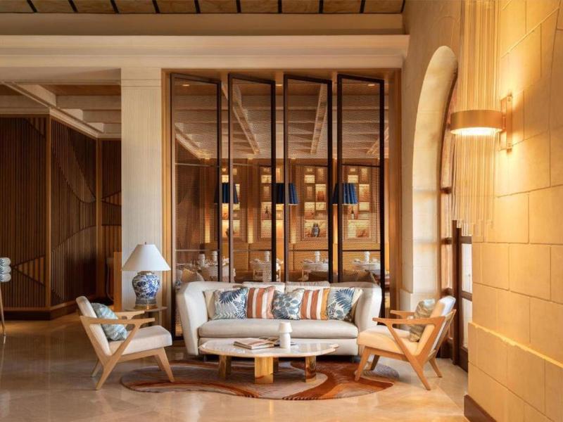 Moderně zařízená hotelová hala s pohovkou, křesly a kulatým konferenčním stolkem v teplých odstínech.