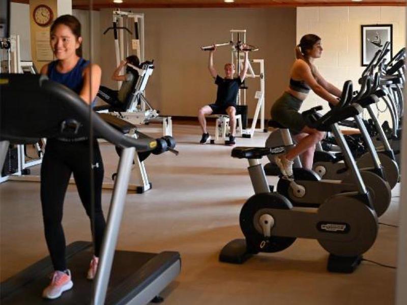 Interiér posilovny s lidmi používajícími běžecké pásy a stacionární kola.