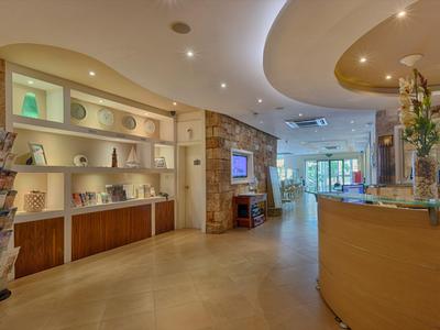 Hall dell'hotel luminosa e moderna con banco reception, scaffali e area salotto sullo sfondo.