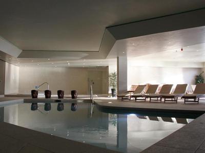 Moderní vnitřní bazén s lehátky a neutrálními stěnami v hotelu.