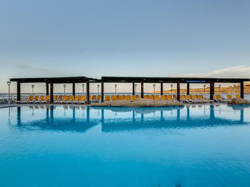 Velký venkovní bazén s moderními stínícími konstrukcemi a žlutými lehátky pod jasnou oblohou.