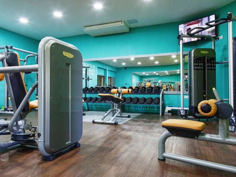 Moderní posilovna s různými tréninkovými stroji a činkami před velkým zrcadlem.