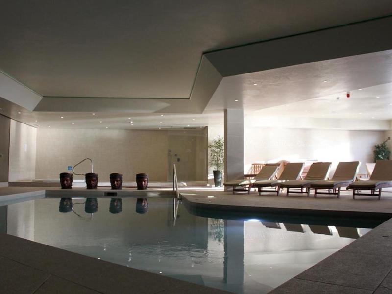 Moderní vnitřní bazén s lehátky a neutrálními stěnami v hotelu.