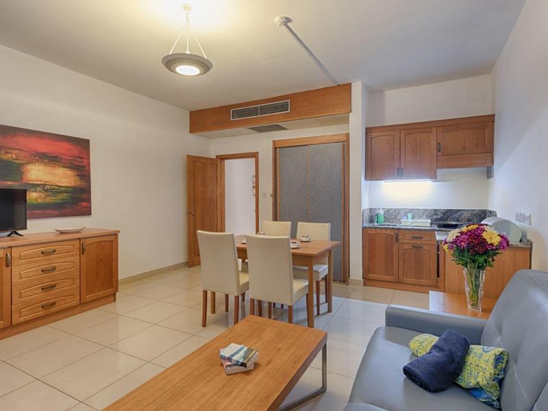 Moderní obývací pokoj s kuchyňským koutem, pohovkou, jídelním stolem a komodou v neutrálních barvách.