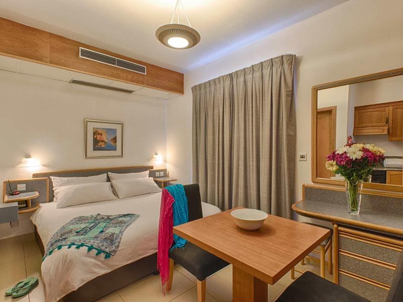 Pohodlný hotelový pokoj s velkou postelí, dřevěným nábytkem a květinovou dekorací.