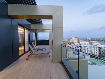 Balcón con sillones y barandilla de vidrio con vistas a la ciudad y el agua al anochecer.