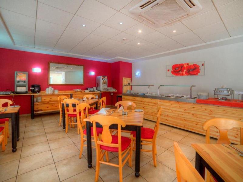 Sala colazione luminosa con tavoli in legno e sedie rosse, buffet lungo la parete.