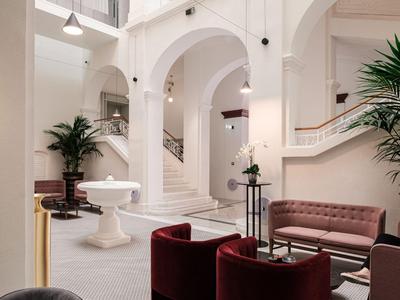 Elegante Hotellobby mit Sitzbereichen, weißen Bögen und großen Zimmerpflanzen.