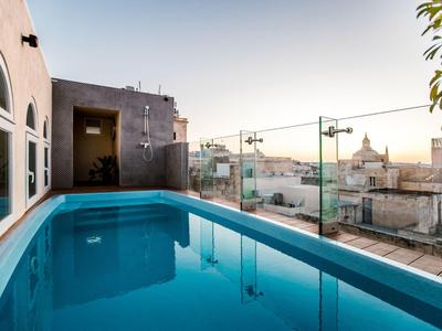 Moderner Dachpool mit Glasgeländer und Blick auf Stadtgebäude bei Sonnenuntergang.