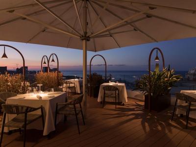 Abendliche Außenterrasse eines Restaurants mit Blick auf das Meer und gedeckten Tischen unter großen Sonnenschirmen.