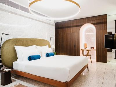 Modernes Hotelzimmer mit großem Bett, zwei Kissen, Holzdetails und einem runden Deckenlicht.