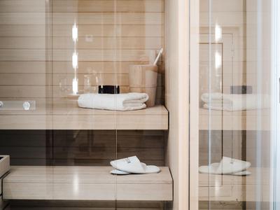 Moderner heller Saunaraum mit Holzverkleidung und weißen Handtüchern und Pantoffeln.