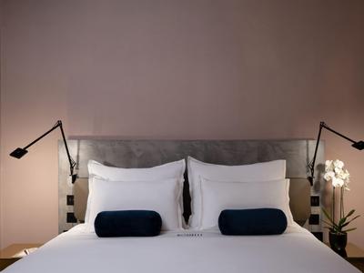 Modernes Hotelzimmer mit großem Bett, weißen Kissen und zwei schwarzen Leselampen.