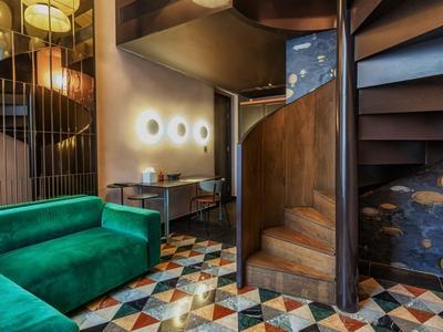 Modern eingerichteter Hotelbereich mit grüner Couch, Spiralholztreppe und gemusterter Fliese