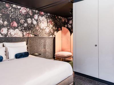 Modernes Hotelzimmer mit floralem Akzent an der Wand, großem Bett und Sessel mit rundem Spiegel.