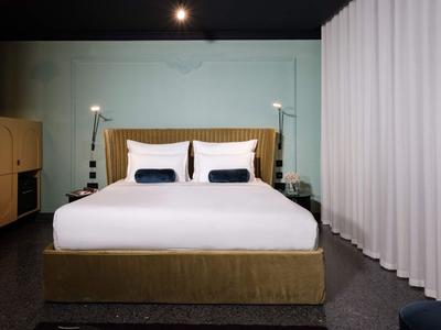 Modernes Hotelzimmer mit großem Bett, weißen Kissen und braunem Kopfteil, umgeben von Vorhängen.