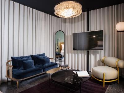 Modern eingerichtetes Hotelzimmer mit dunkelblauem Sofa, Sessel und einem großen Spiegel.