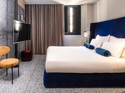 Modernes Hotelzimmer mit großem Bett, blauen Akzenten und gemütlichem Sitzbereich.