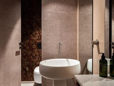 Modernes Badezimmer mit rundem Waschbecken, großem Spiegel und beleuchteter dusche im Hintergrund.