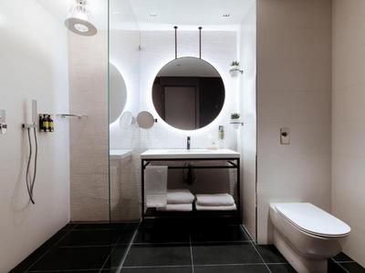 Modern hotel bathroom with round backlit mirror, glass shower, and wall-mounted toilet.