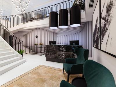 Moderno vestíbulo de hotel con escalera, mostrador negro y sillones verdes.