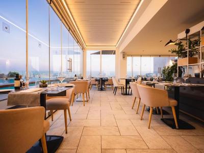 Restaurante moderno con grandes ventanales y vista a la piscina al atardecer.