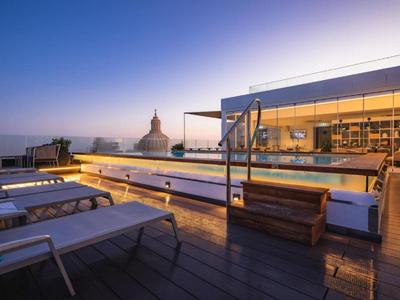 Dachterrasse mit Pool, Liegestühlen und Blick auf eine historische Kuppel bei Abendlicht.