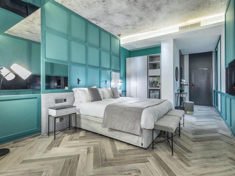 Modern hotel room with teal paneled walls, large bed, and herringbone wood floor.