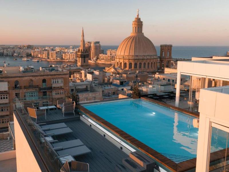 Rooftop pool with city view during sunset, featuring dome and spire buildings.