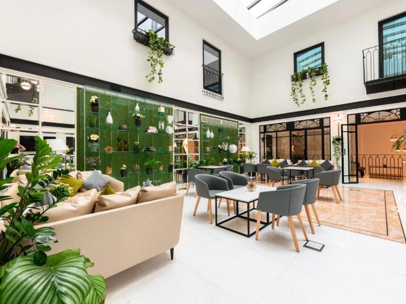 Bright hotel lounge with green wall, beige sofa, gray chairs, and large windows letting in natural light.