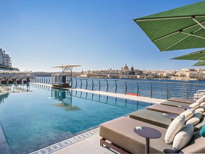 Piscine moderne avec transats et vue sur une ville au bord de l'eau sous un ciel clair
