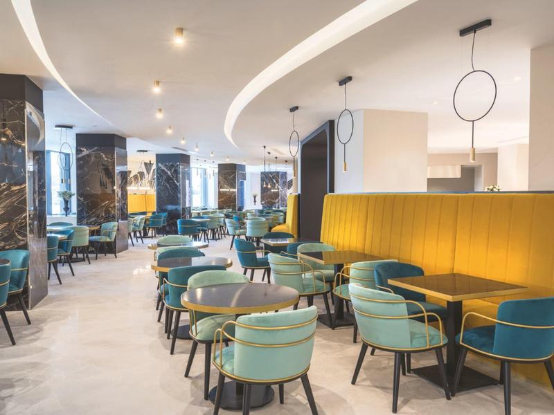 Restaurant moderne avec des chaises turquoise et un canapé jaune sous des lumières de plafond rondes.