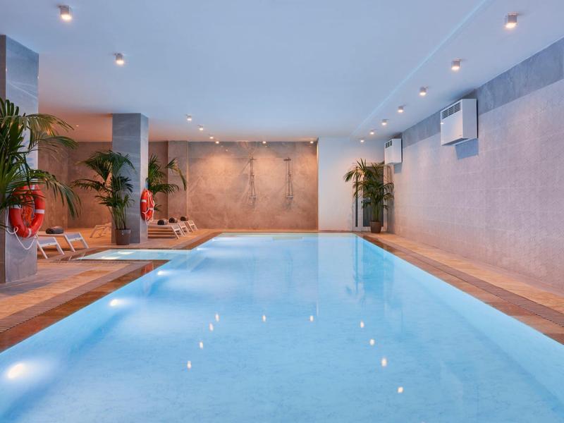 Piscine intérieure moderne avec terrasse en bois et plantes dans un cadre élégant.