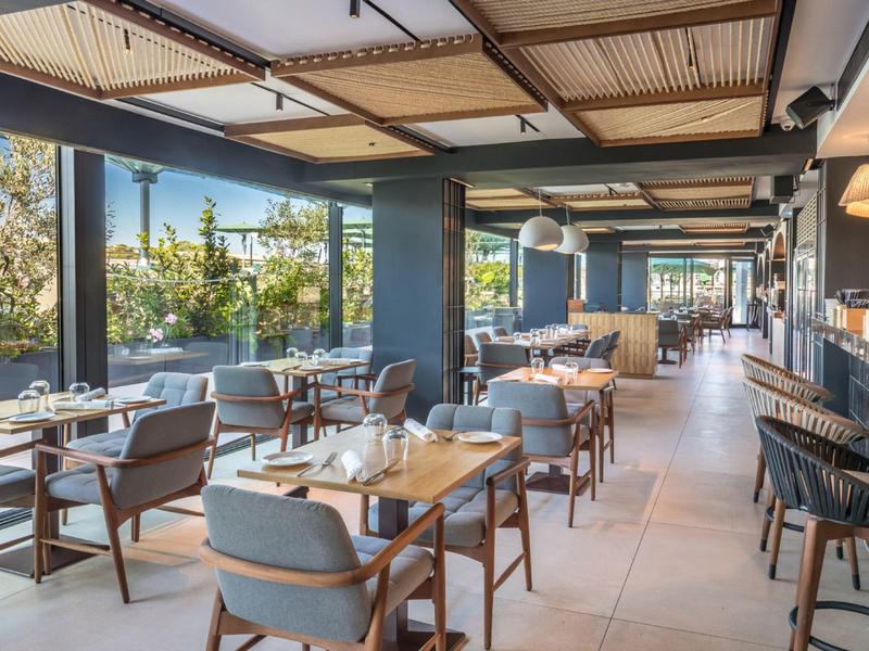 Restaurant moderne avec des tables, des chaises et de grandes fenêtres donnant sur la nature.