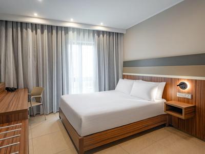 Habitación de hotel moderna con cama doble grande, escritorio y cortinas frente a una ventana.