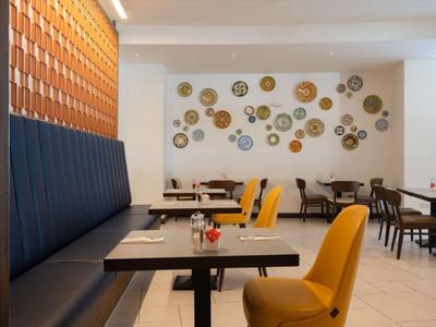 Área de comedor moderna con sillas amarillas, bancos azul oscuro y objetos decorativos en la pared.