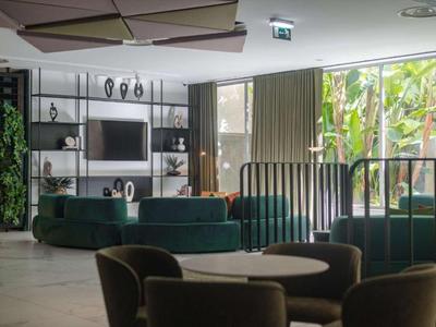 Área de lounge de hotel decorada de forma moderna con sillones, sofás y grandes ventanas con vistas al verde.