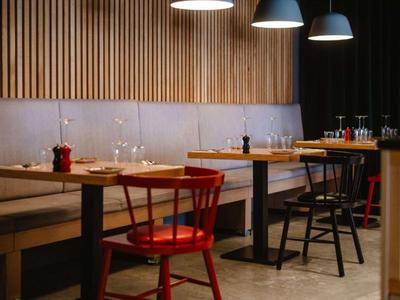 Área de comedor moderna con mesas de madera, sillas negras y rojas, y paneles de pared de madera