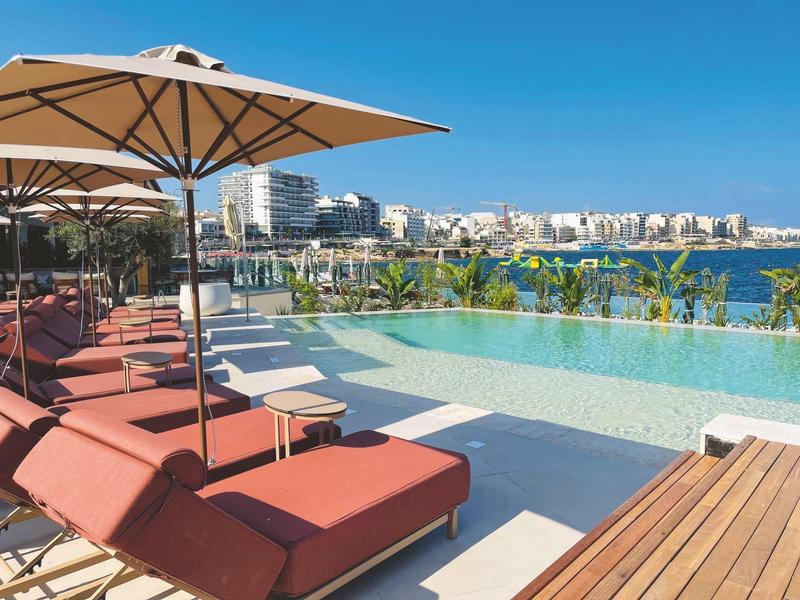 Área de piscina con tumbonas rojas y vista clara al mar
