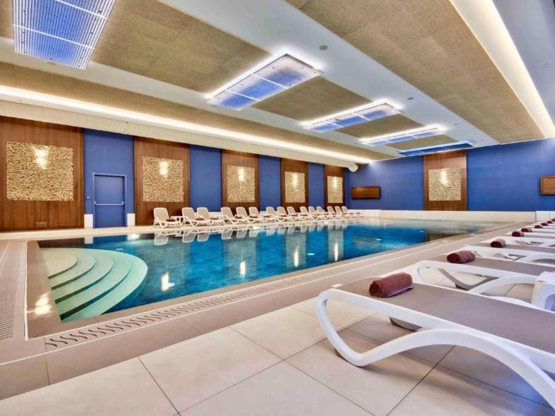 Piscina interior moderna con tumbonas y diseño de iluminación brillante en un hotel.