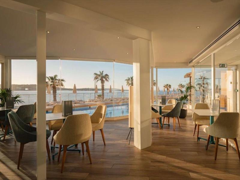 Área de comedor luminosa con vista a la piscina y al mar al atardecer.
